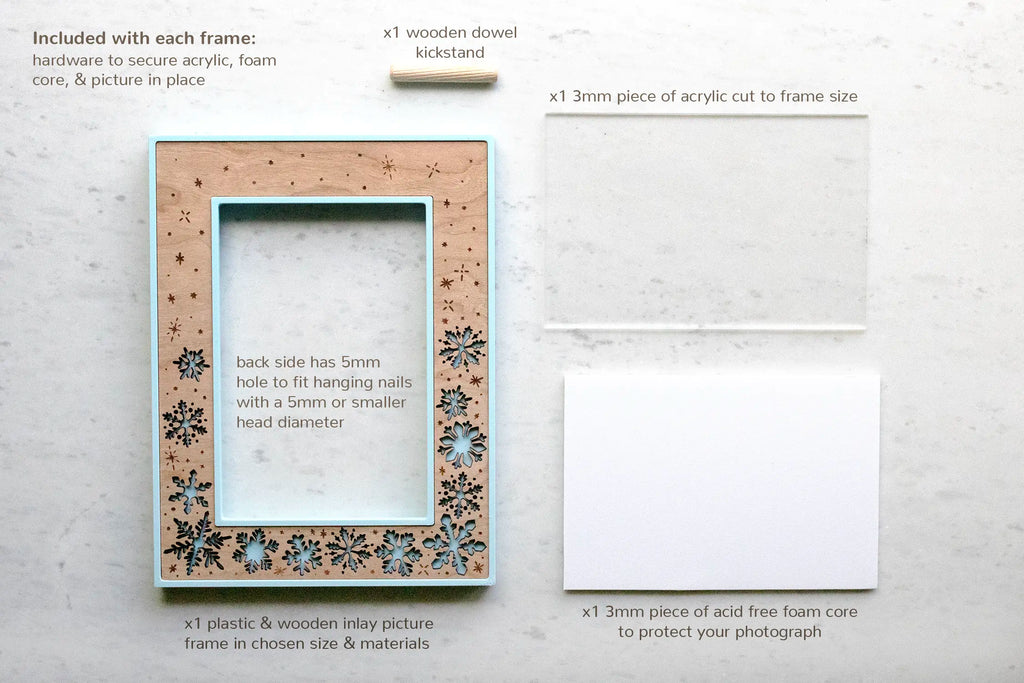 A flat-lay showing everything included with the laser-cut snowflake picture frame: the laser-cut frame itself (ice-blue housing, cherry wood inlay), a 3mm piece of frame-grade acrylic, a 3mm acid-free foam-core backing to keep photos from yellowing, a wooden dowel kickstand, and hardware to hold it all in place. The back has a 5mm hole for hanging on a nail.