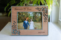 An elegant floral wood frame for a wedding keepsake. The frame is cherry wood and sage green with a delicate floral design around the border. The picture frame holds a 5x7 photograph, and it has a horizontal orientation. The frame displays a photograph of a couple at their wedding.
