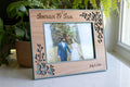 A delicate floral wood frame for a wedding keepsake. The frame is cherry wood and sage green with a delicate floral design around the border. The green frame is 3D printed, and the wooden decorative inlay is laser cut from real wood. The frame is sitting on a white marble surface.