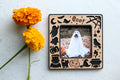 Magnetic Halloween picture frame sized for Polaroid photos with wooden inlay and engraved text "Boo!". The frame features cute ghosts, pumpkins, black cats, spiders, a raven, and a witch's hat, broomstick, and cauldron.