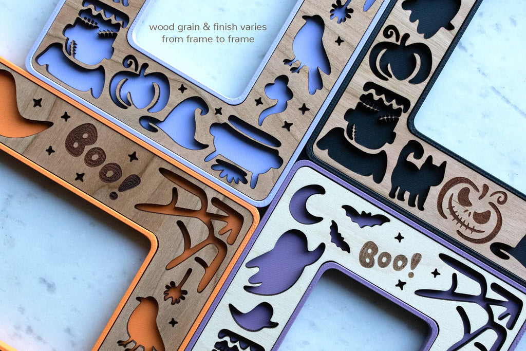 Close-up view of purple, orange, and black mini Halloween picture frames with magnets. Frames feature black cats, Frankenstein, pumpkins, ghosts, and a starry night sky with moon and stars.