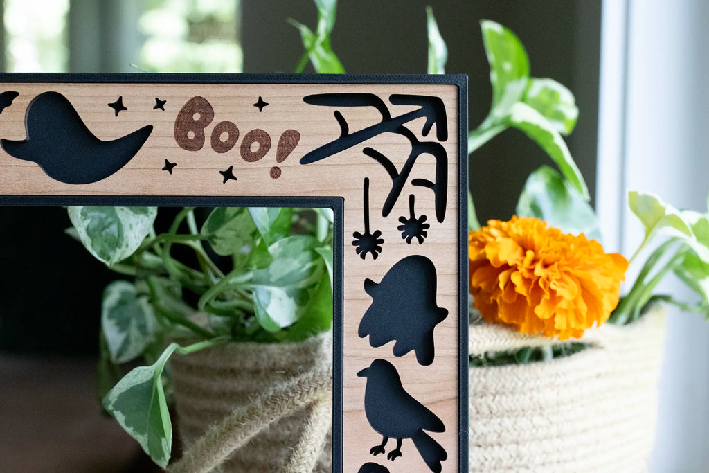Close-up, detail view of custom laser cut Halloween picture frame with cute spiders, spiderweb, ghosts, and a raven in the top-right corner.