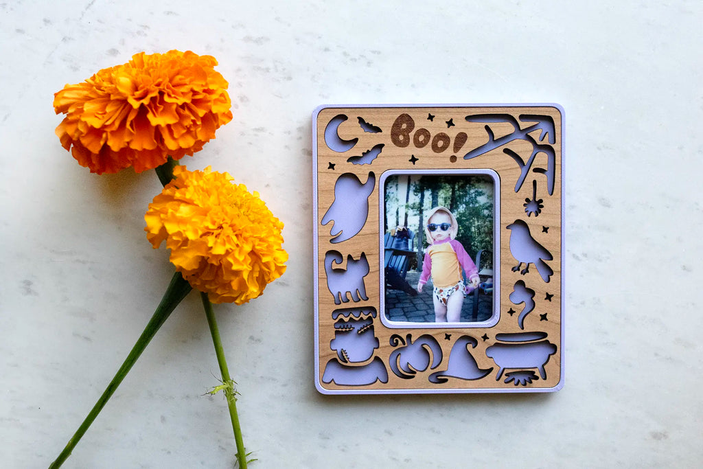 Instax Mini Halloween picture frames with magnets for refrigerator Halloween decor. Frame is purple with a cherry wood inlay and has orange flowers lying next to it.