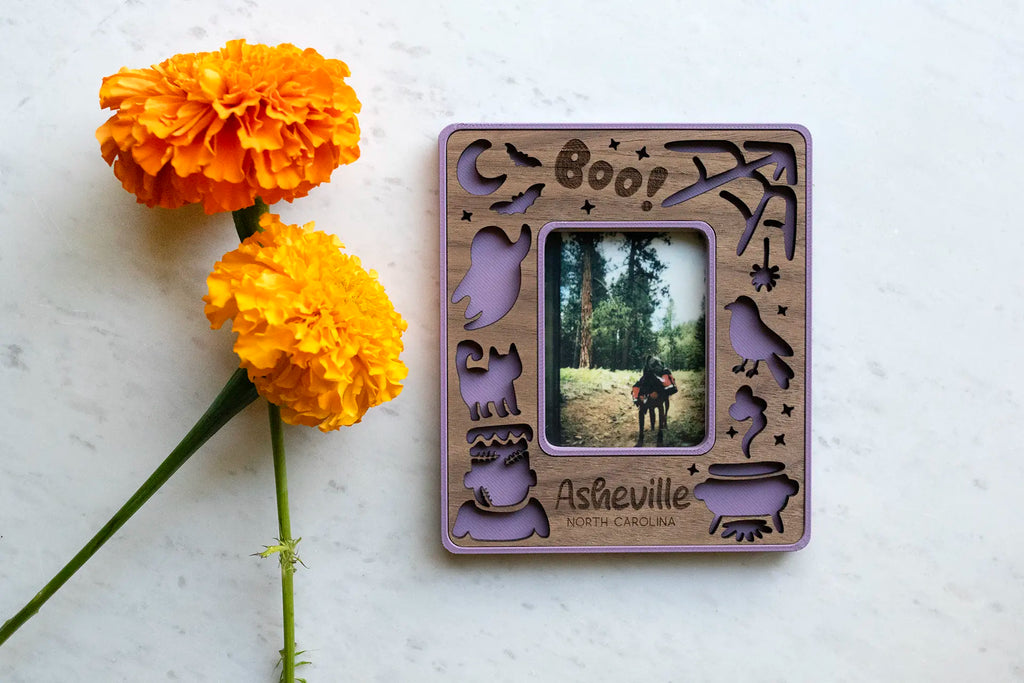 Purple Instax mini magnetic frame with Halloween design, including laser-cut ghosts, pumpkins, cute Frankenstein, witch's cauldron, broomstick, and witch's hat. The frame displays an Instax Mini photo of a dog with a backpack.