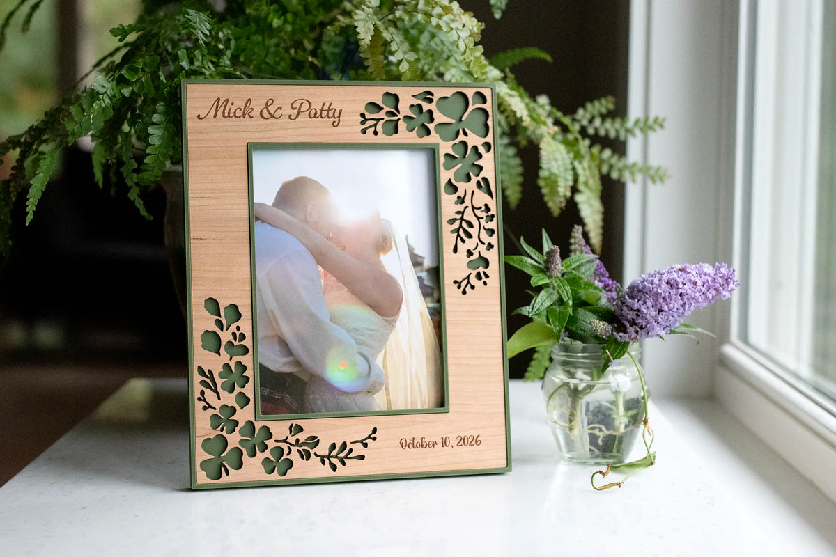 Personalized Irish wedding shamrock picture frame, laser-cut clover in cherry wood over moss green, displaying a bride and groom's wedding photo, engraved "Mick & Patty, October 10, 2026".