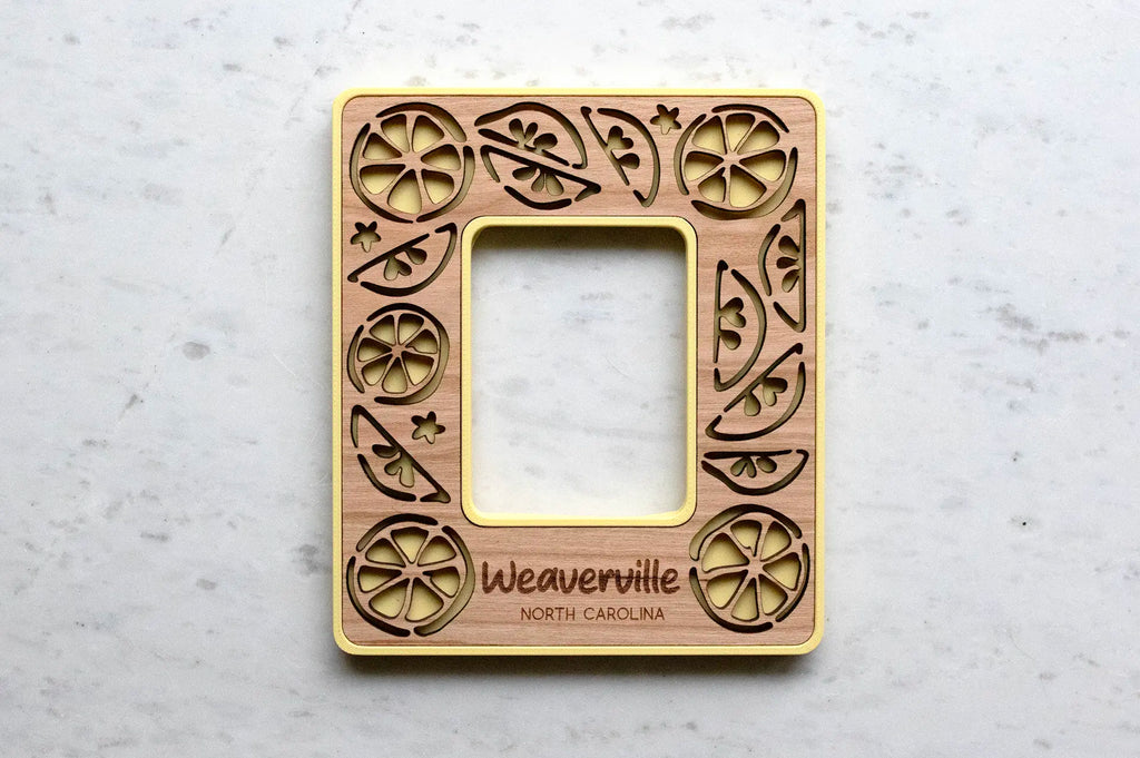 Personalized lemon picture frame for Instax Mini photos. Frame is yellow with a cherry wood inlay and the words "Weaverville North Carolina" engraved.