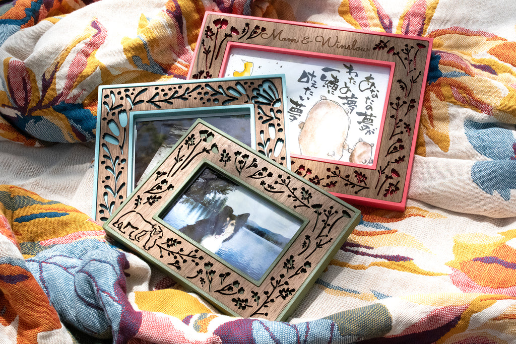 Three wooden picture frames with a laser-cut floral pattern and colorful 3D printed border. Frames are fully customizable with a name or unique message. 5x7 frames, 4x6 frames, ultrasound frames, and Polaroid frames are available sizes.