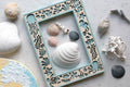 Handmade keepsake ocean creatures picture frame featuring laser-cut marine motifs including jellyfish, seahorses, crabs, and seaweed. Several seashells of varying sizes, shapes, and colors are arranged around and inside the frame.