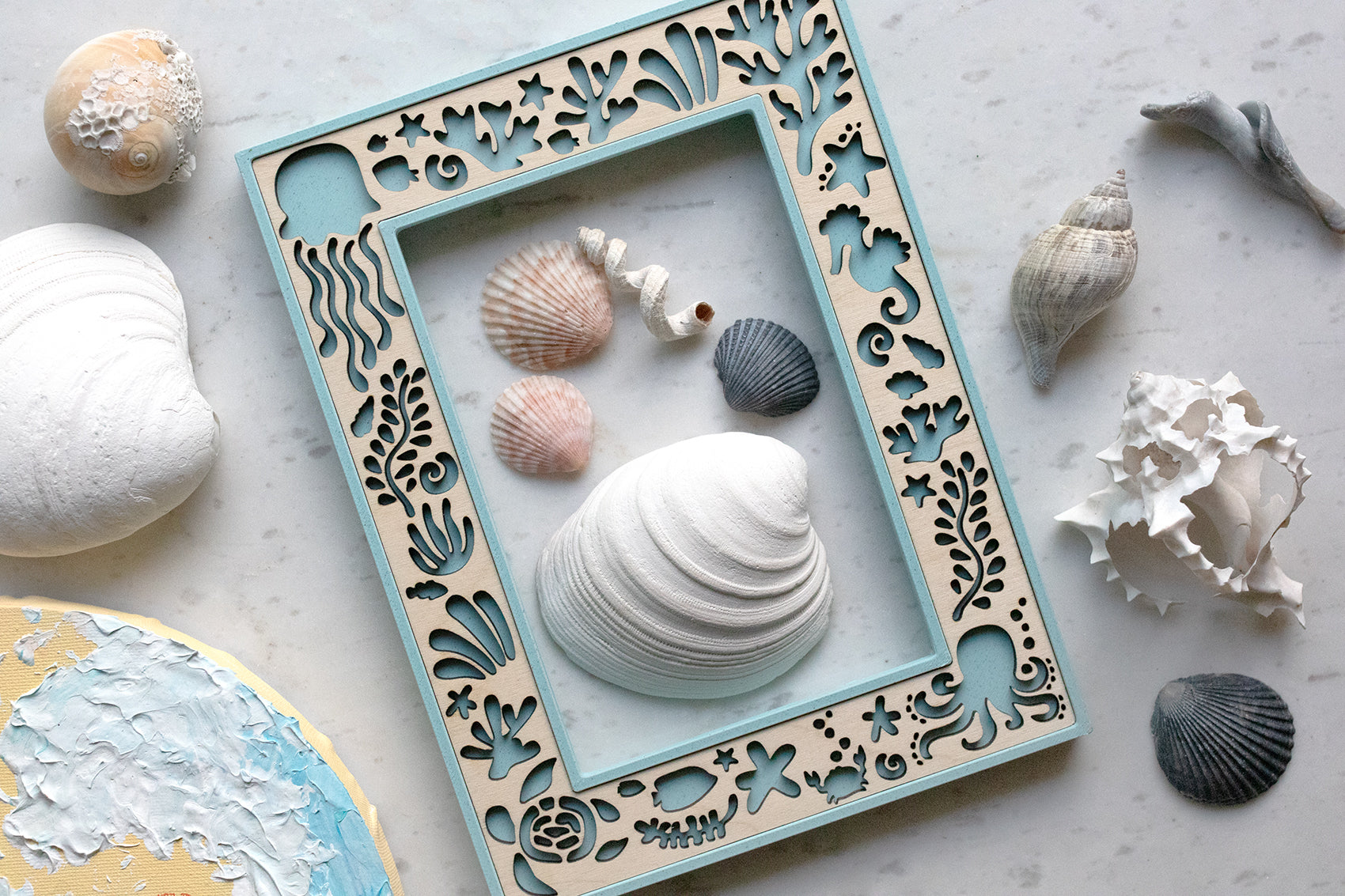 Handmade keepsake ocean creatures picture frame featuring laser-cut marine motifs including jellyfish, seahorses, crabs, and seaweed. Several seashells of varying sizes, shapes, and colors are arranged around and inside the frame.