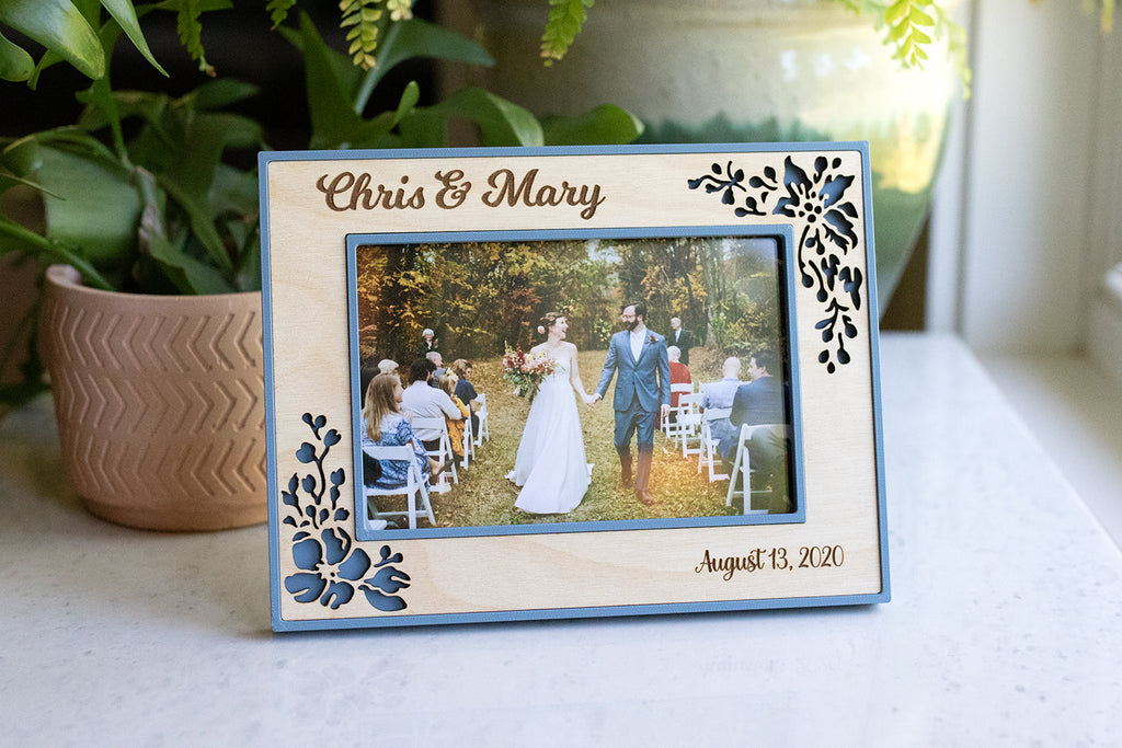 A 4x6 picture frame in slate blue and light maple wood floral inlay. The design is delicate and feminine for a wedding gift or wedding keepsake. The frame displays a photograph of a couple at their wedding ceremony.