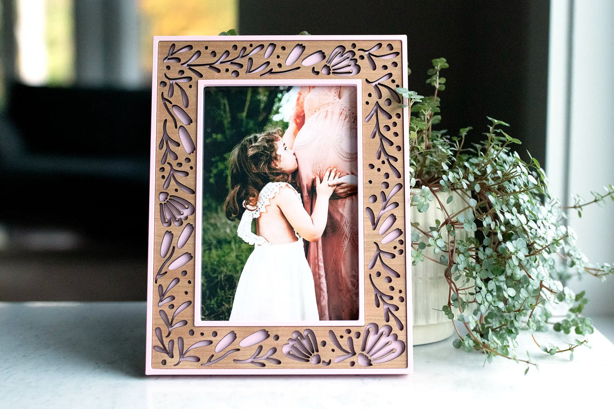 Camellia Pink flower picture frame with a laser-cut cherry wood inlay holding a maternity photo of a little girl kissing her pregnant mother’s belly.