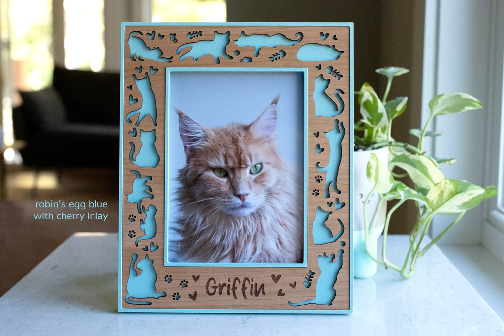 Personalized cat memorial picture frame in cherry wood with laser-cut cat silhouettes, paw prints, robin’s egg blue housing, and engraved name.