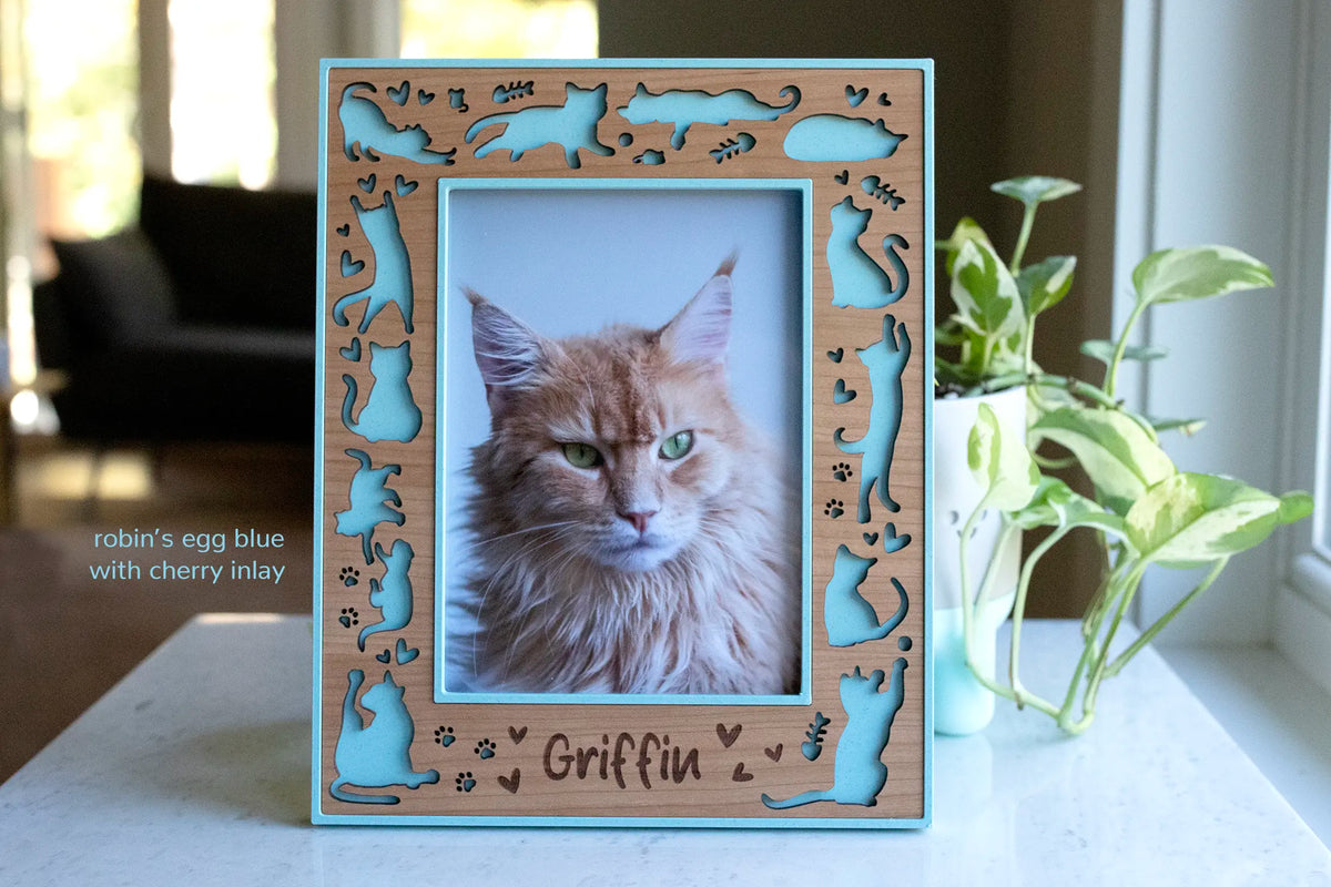 Personalized cat memorial picture frame in cherry wood with laser-cut cat silhouettes, paw prints, robin’s egg blue housing, and engraved name.