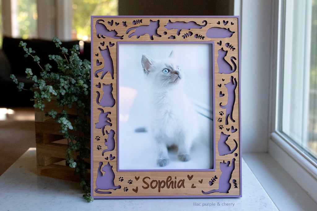 Personalized cherry wood cat frame with lilac purple edging, engraved pet name, and laser-cut cat, paw print, heart, and fish cutouts, holding a photo of a Siamese kitten.