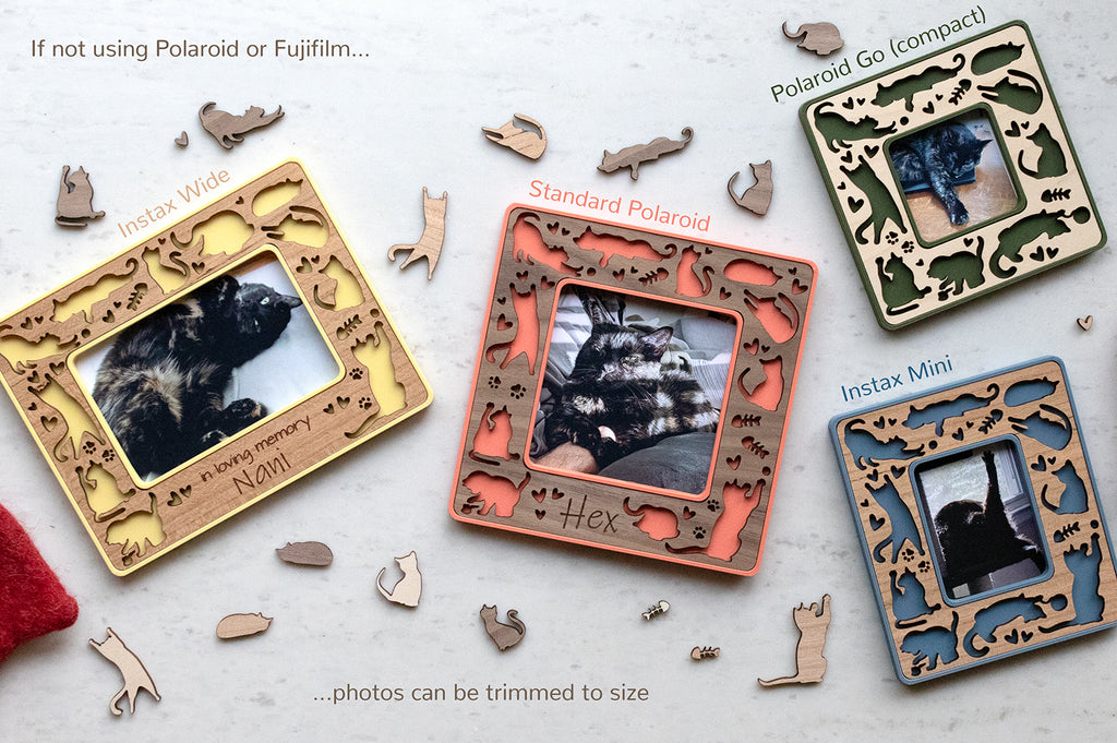 Small magnetic cat frames featuring cute laser cut cat designs, cat paw prints, and fish bones. The frames come in four sizes: Instax Wide, Instax Mini, Standard Polaroid, and Polaroid Go. Frames are yellow, coral pink, blue, and green with various wooden inlays. The image has a note that reads "If not using Polaroid or Fujifilm, photos can be trimmed to size."  The frames are surrounded by tiny laser cut wooden cats.
