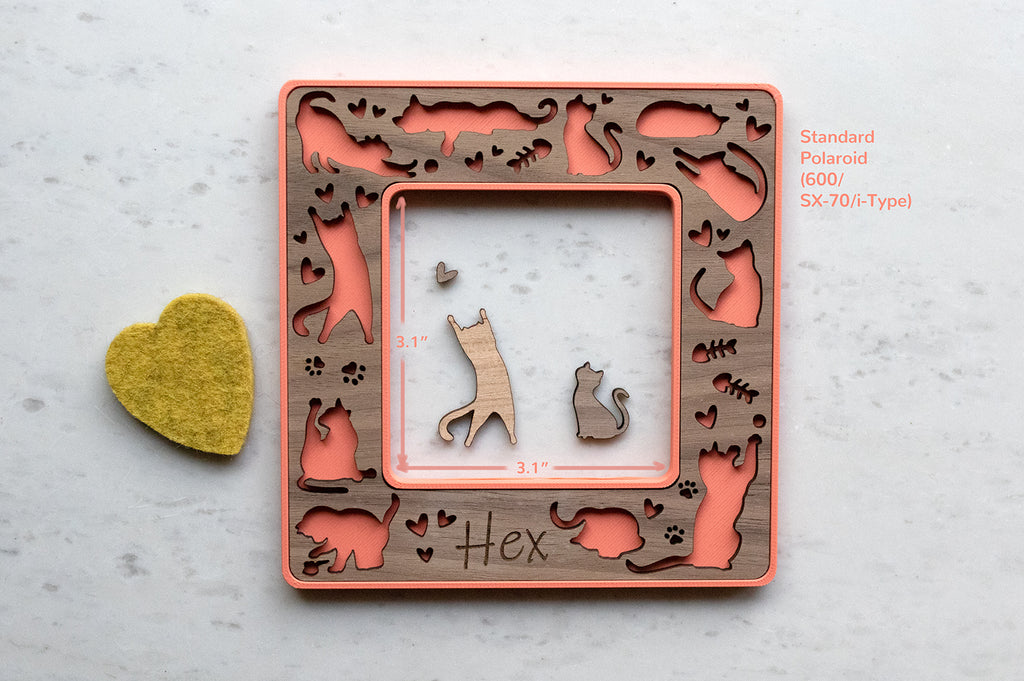 A bright coral pink magnetic cat frame in standard polaroid size with the name "Hex" engraved on the bottom. Standard Polaroid is also known as 600, SX-70, iType. The frame features a laser cut cats design with hearts, little fish bones, and kitty paw prints. The photo opening in the frame is 3.1" x 3.1".
