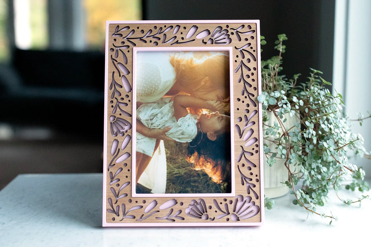Cherry wood flower inlay picture frame in Camellia Pink holding a sunlit photo of a mother lifting her laughing daughter.