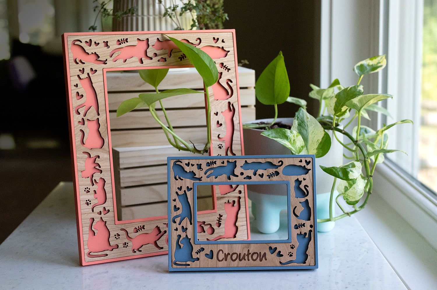 Two cute, laser engraved cat frames with custom cat names. The frames pictured are a 5x7 cat frame and an Instax Wide frame. They are coral pink and slate blue with cherry wood inlays.