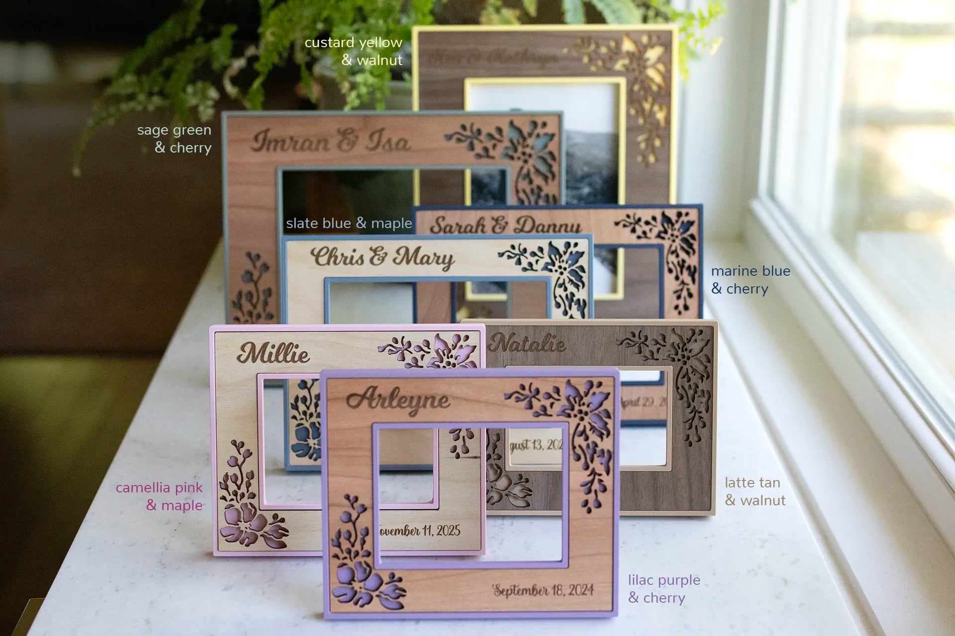 An assortment of wedding photo frames with floral designs in pale yellow, sage green, and various shades of blue. Also pictured are a polaroid frame and an ultrasound frame in shades of pink and purple. All frames are customizable with engraved names, dates, and wood styles.