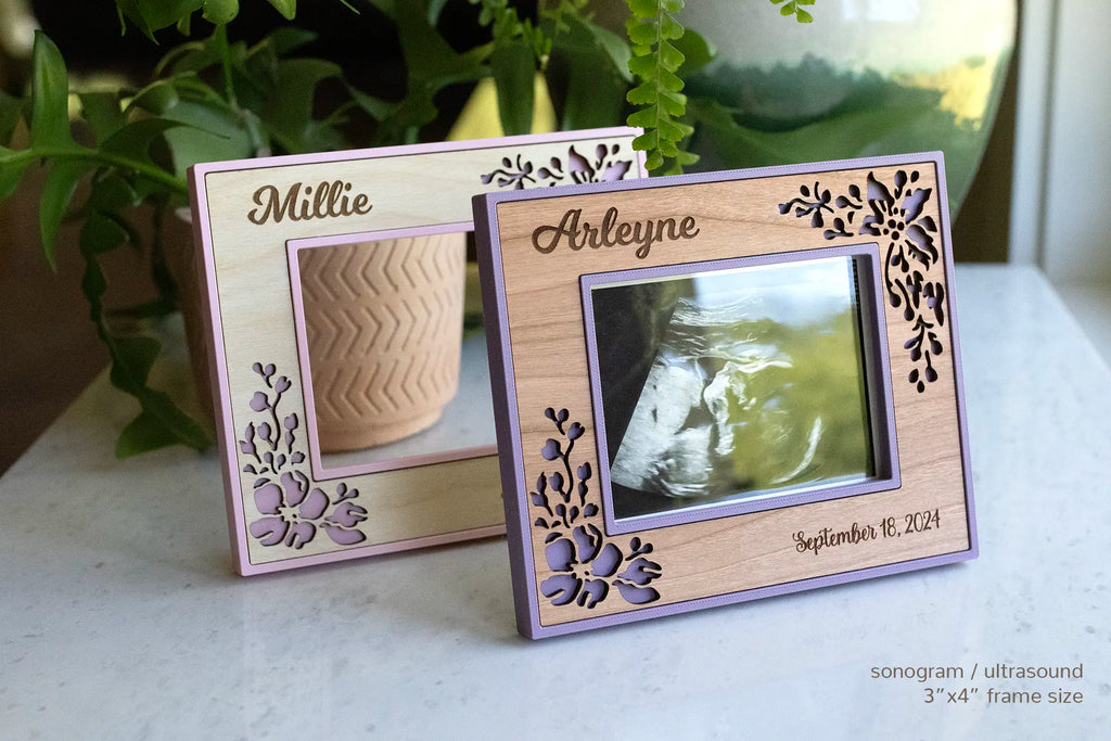 Two ultrasound frames in pink with a floral maple design and purple with a floral cherry design. The front floral frame displays an ultrasound photo. This frame style makes a great gift for new mom.