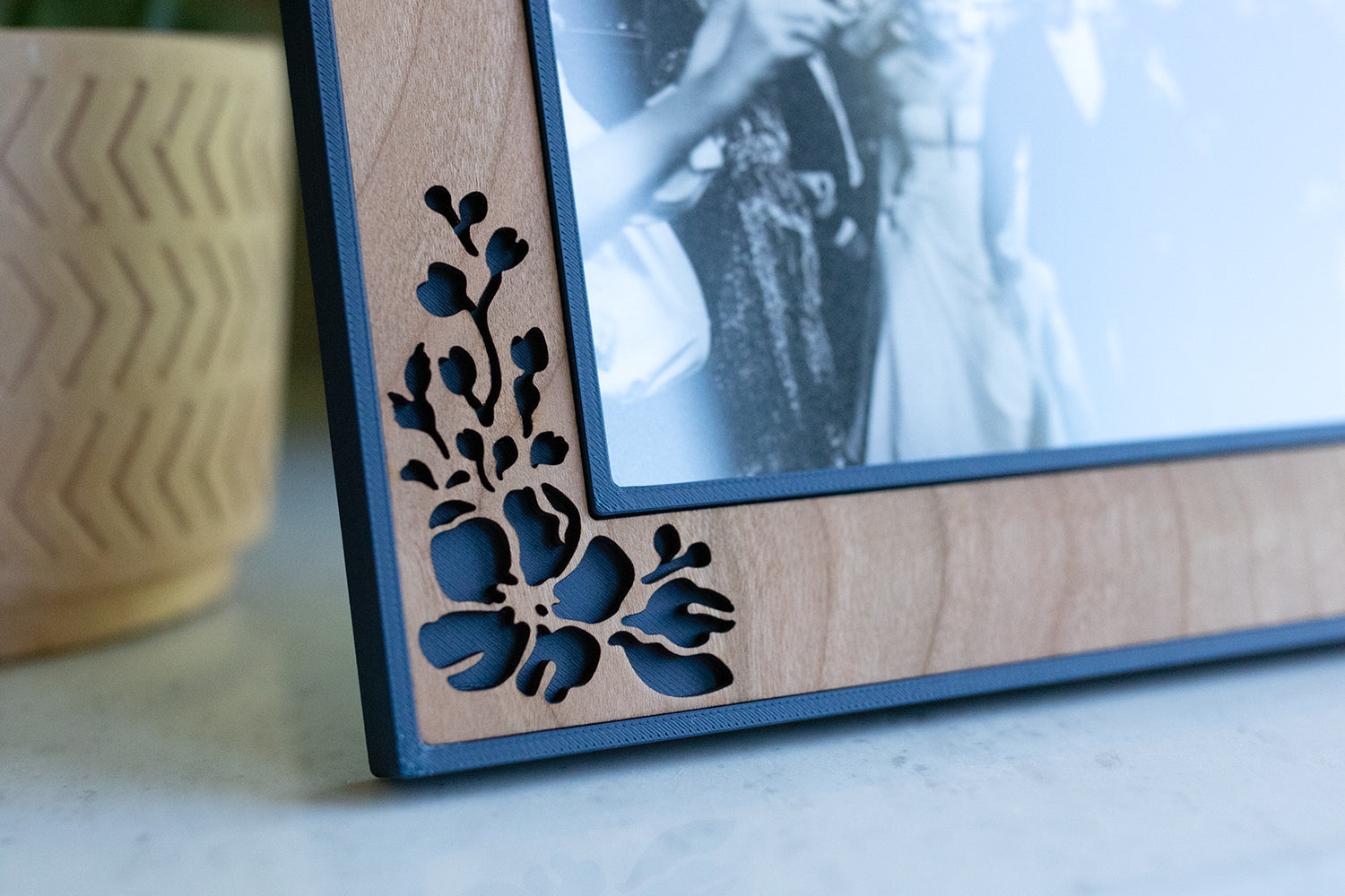 A close-up detail view of a wooden frame with delicate laser cut flowers and a navy blue picture frame backing. The natural cherry wood grain makes this wedding frame a special gift for a loved one.