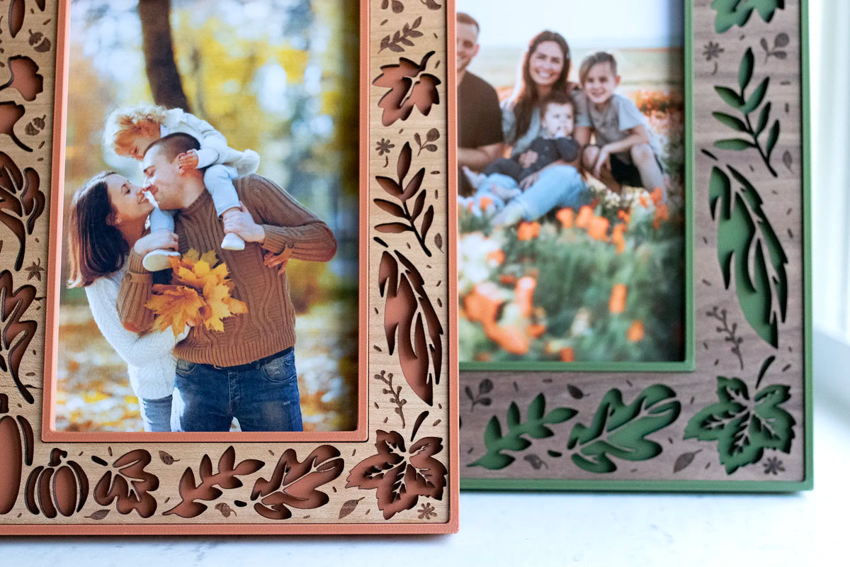 Close-up of 4×6 and 5×7 fall leaf picture frames — terracotta with a cherry wood inlay and moss green with a walnut inlay. These handcrafted fall frames feature laser-cut oak and maple leaves, pumpkins, acorns, and berries, displaying autumn family portraits.