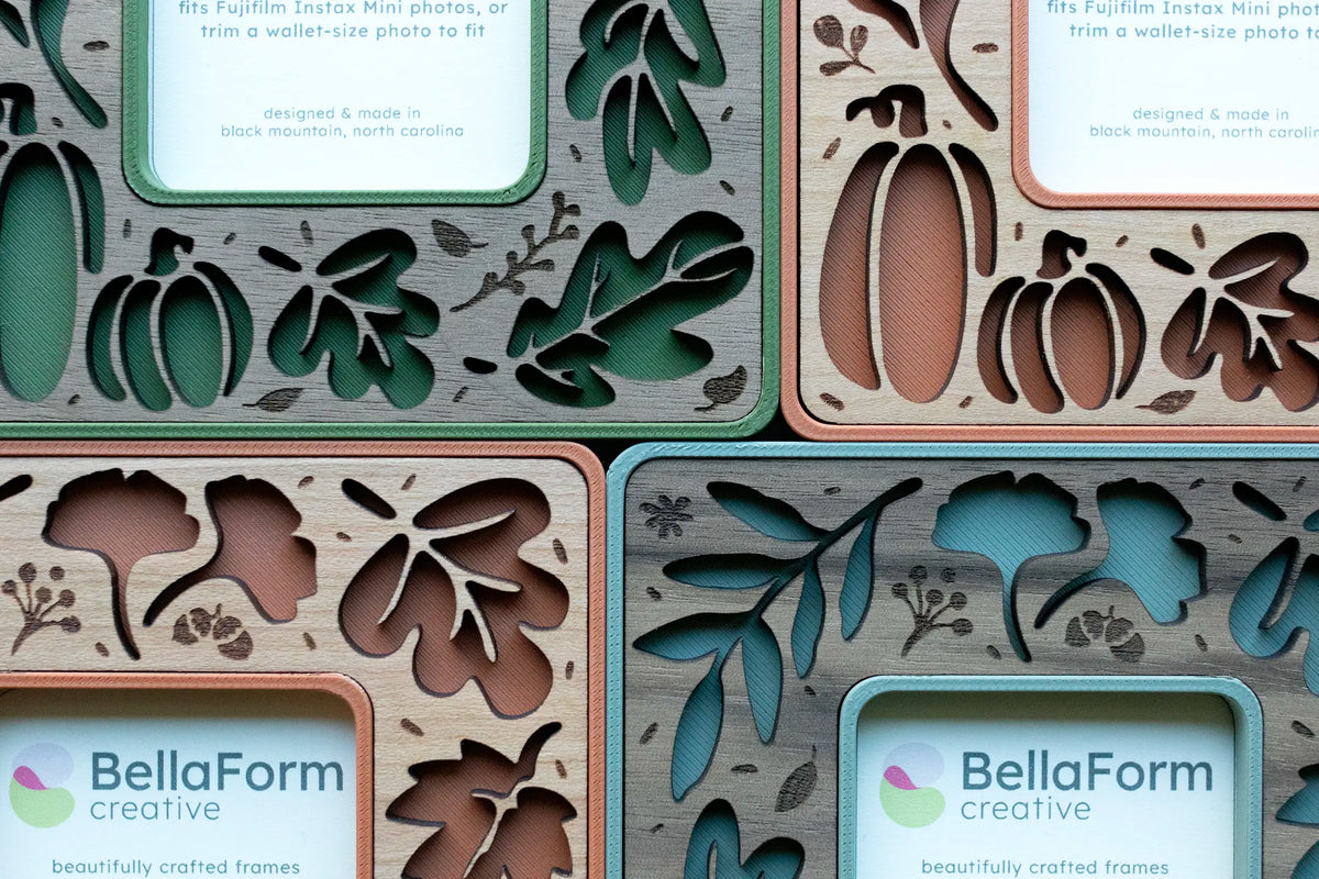 Close-up detail of fall leaves magnetic frames in moss green, sage green, and terracotta with walnut and cherry wood inlays, showing laser-cut pumpkin, ginkgo, and autumn leaf cutouts with engraved acorn and berry accents.