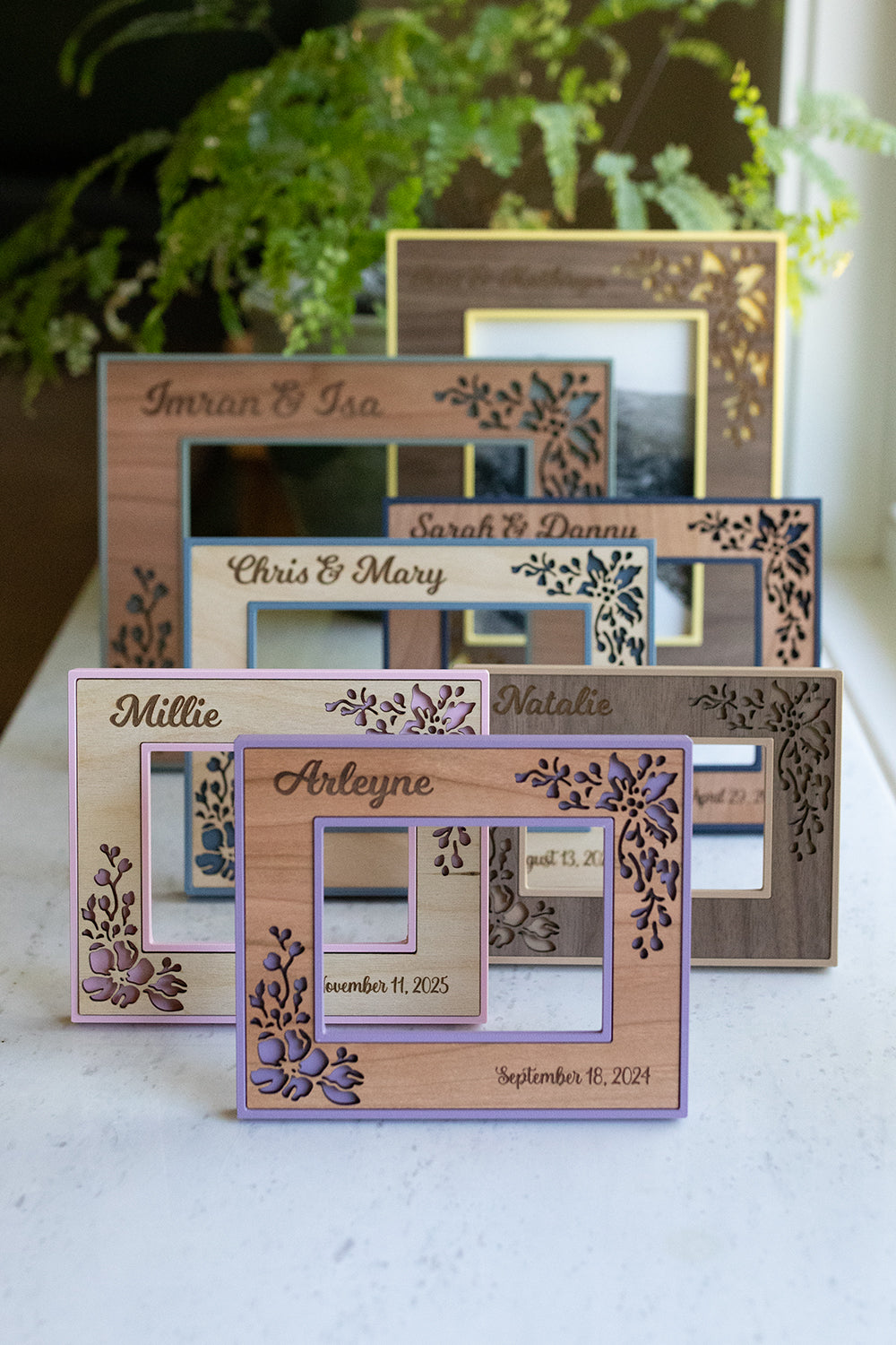 An assortment of wedding photo frames in pale yellow, sage green, and various shades of blue. Also pictured are a polaroid frame and an ultrasound frame in shades of pink and purple. All frames are customizable with engraved names, dates, and wood styles.