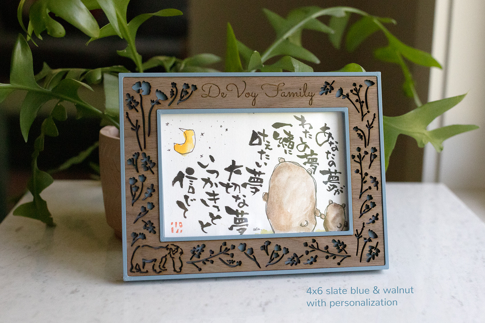 A 4x6 slate blue and walnut picture frame displaying a watercolor illustration of bears holding hands and Japanese calligraphy. The frame has a decorative floral and laser cut bear design. The frame is personalized with the words "DeVoy Family" in delicate script across the top.