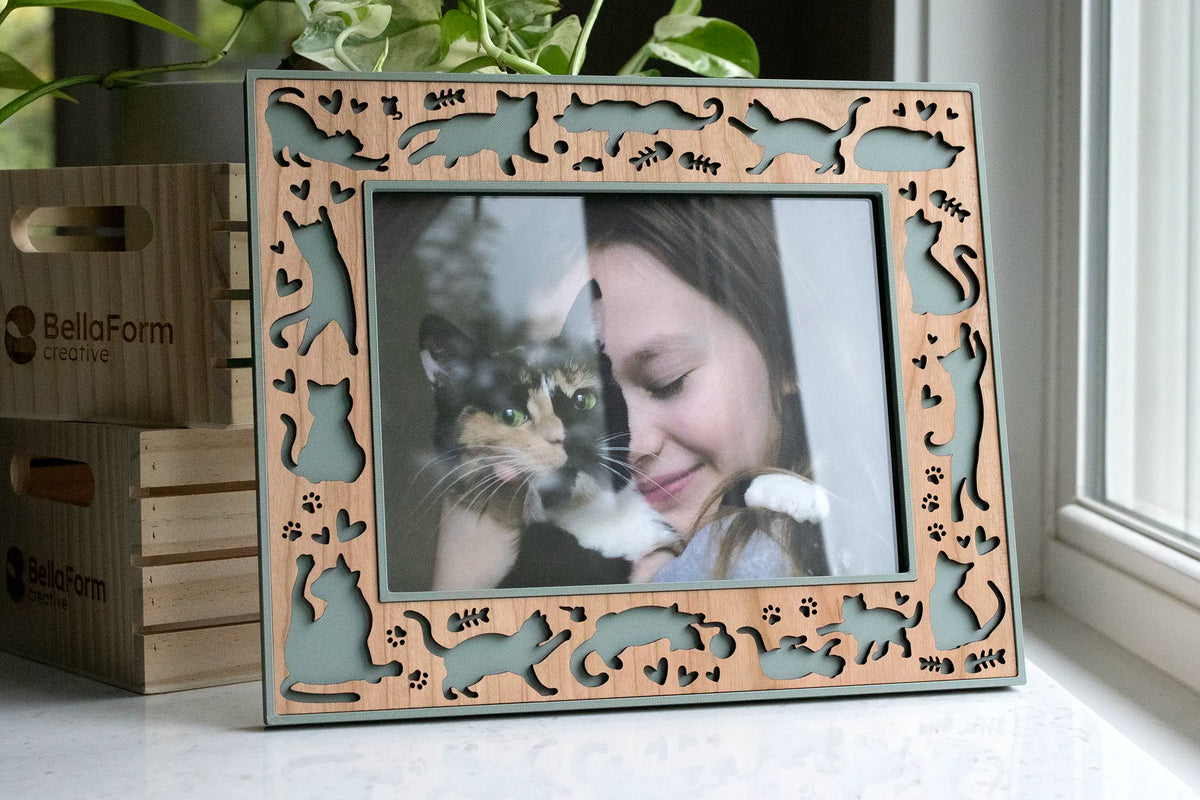 A laser-cut cat keepsake from with cherry wooden inlay and sage green frame. The frame is 6x8 landscape orientation and displaying a photo of a girl hugging her calico cat.