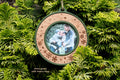 Christmas picture frame ornament in moss green with a cherry inlay, laser-engraved with snowflakes and falling snow and no text, holding a photo of a family of four hugging outdoors, hanging on evergreen branches.