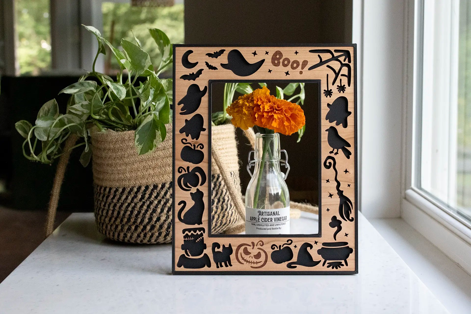 Halloween picture frame featuring ghosts, pumpkins, bats, spiders, and black cats. This 5x7 laser cut picture frame includes an engraved "Boo!" message and laser cut spider web, witch's hat, witch's broom, and a bubbling cauldron. Halloween keepsake to store halloween memories.