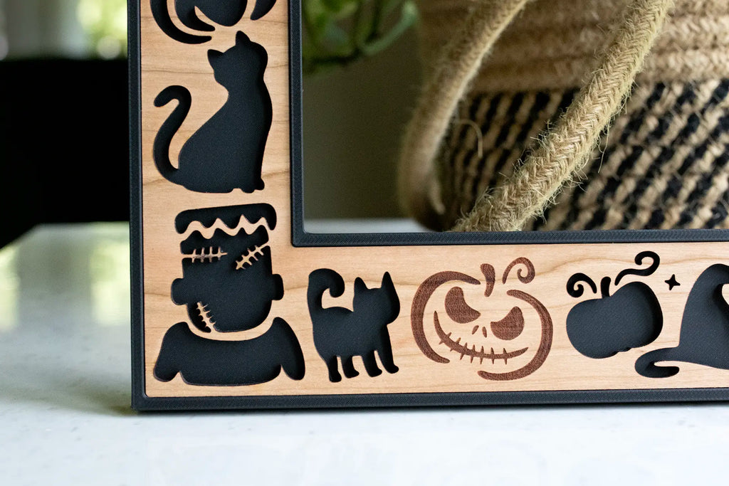 Close-up, detail view of custom laser cut Halloween picture frame with cute Frankenstein, black cats, and pumpkins in the bottom-left corner.
