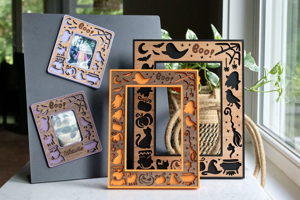 Hand crafted Halloween picture frame in laser-cut wood — black cats, bats, ghosts, pumpkins, and a "Boo!" design around the photo opening. Available in black, orange, and purple.