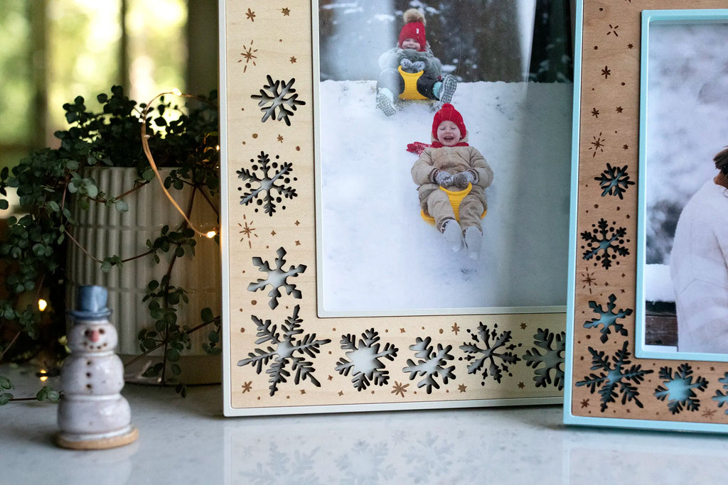 Close-up view of a handmade laser-cut holiday frame with falling snowflakes. This large 5x7 frame is displaying a picture of kids sledding in the snow. Frames can be personalized with your own engravings or left text-free for snowflake-only designs.