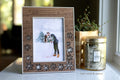 Laser cut snowflake picture frame with personalized "2026" engraved in the top left corner. Frame is linen white with a walnut wood inlay, featuring delicate snowflakes and displaying a photo of a couple at their winter wedding.