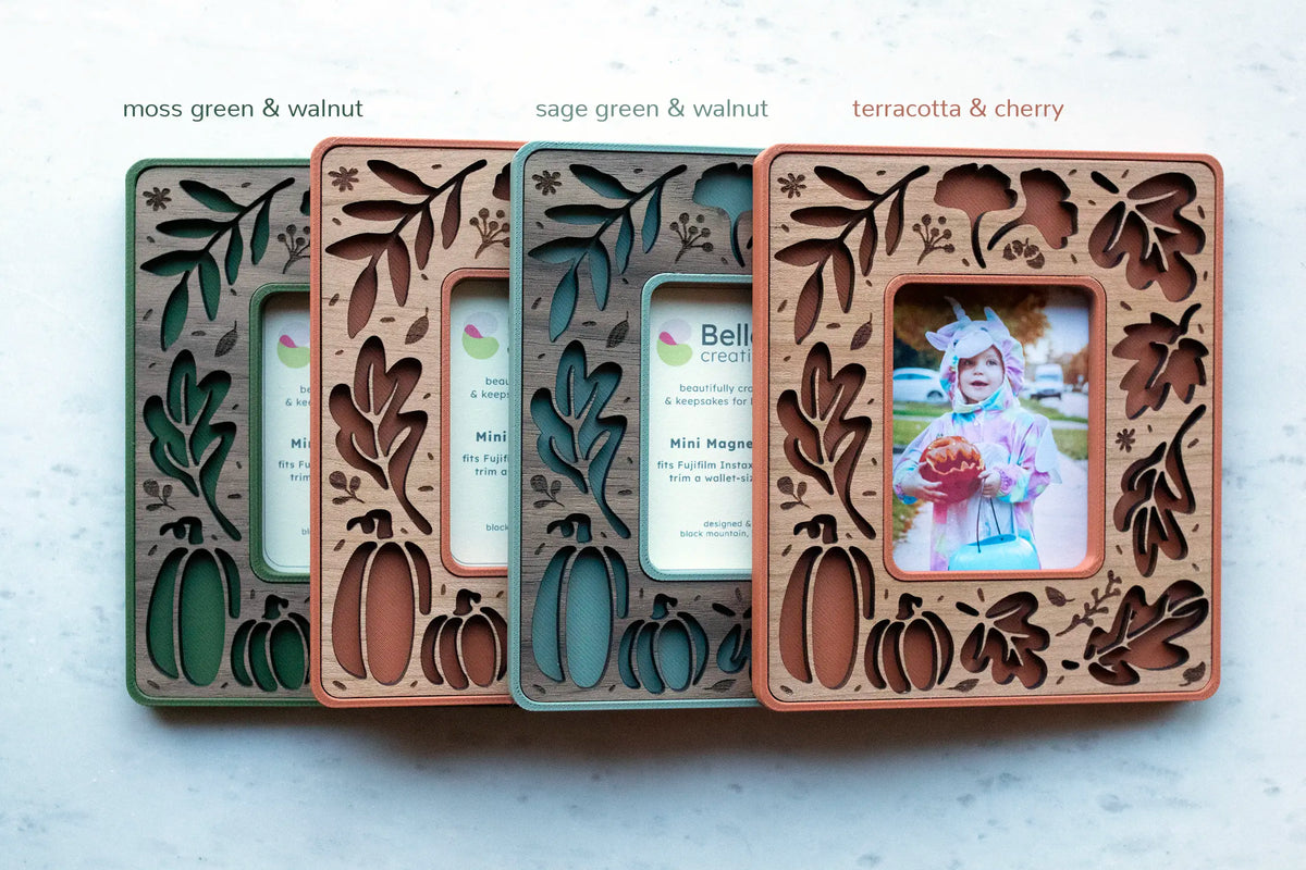 Four fall leaves magnetic frames lined up to show color options, including moss green and walnut, sage green and walnut, and terracotta and cherry, with laser-cut autumn leaf and pumpkin cutouts.