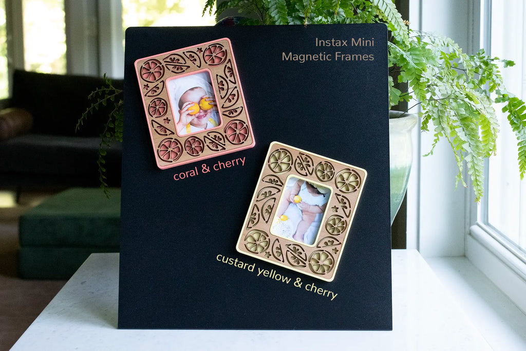Two citrus magnetic picture frames with cute lemons and lemon slices and wedges in a laser-cut design. Frames are custard yellow and coral with cherry wood inlays. These Instax Mini magnetic frames make great small gifts for lemon lovers and kitchen decor.