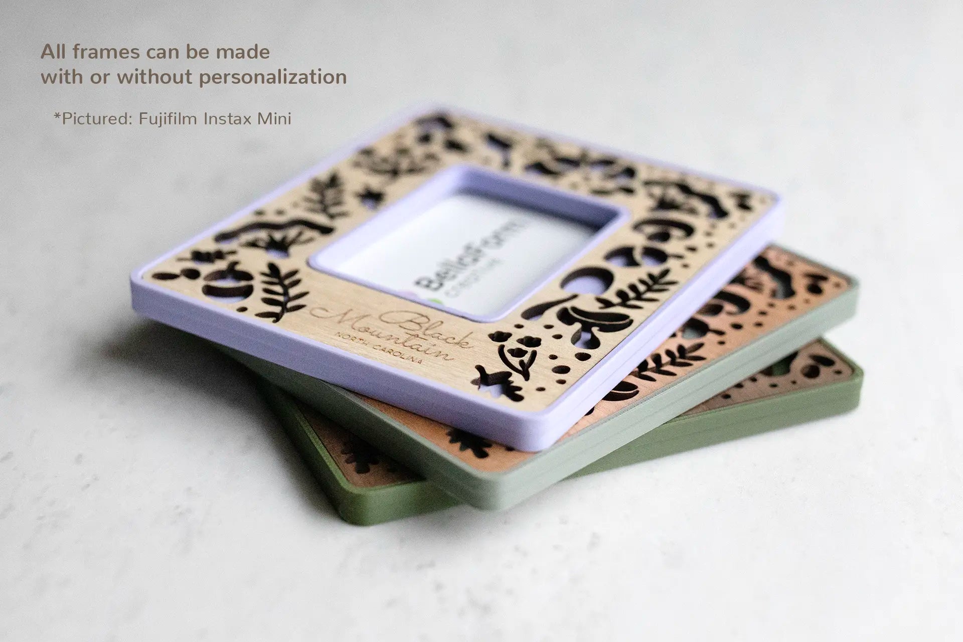 Three Instax Mini magnetic Polaroid photo frames with mushroom designs stacked on top of each other. The top left corner of the image displays the words: "All frames can be made with or without personalization". The frames pictured feature three colors and wood types: periwinkle purple with maple inlay, sage green with cherry inlay, and moss green with walnut inlay.