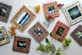 An assortment of colorful, laser cut Polaroid frames with mama and baby bear woodlands design. The frames are lying on a white surface, surrounded by flowers from the garden. They have an intricate, feminine design and real wooden inlays.