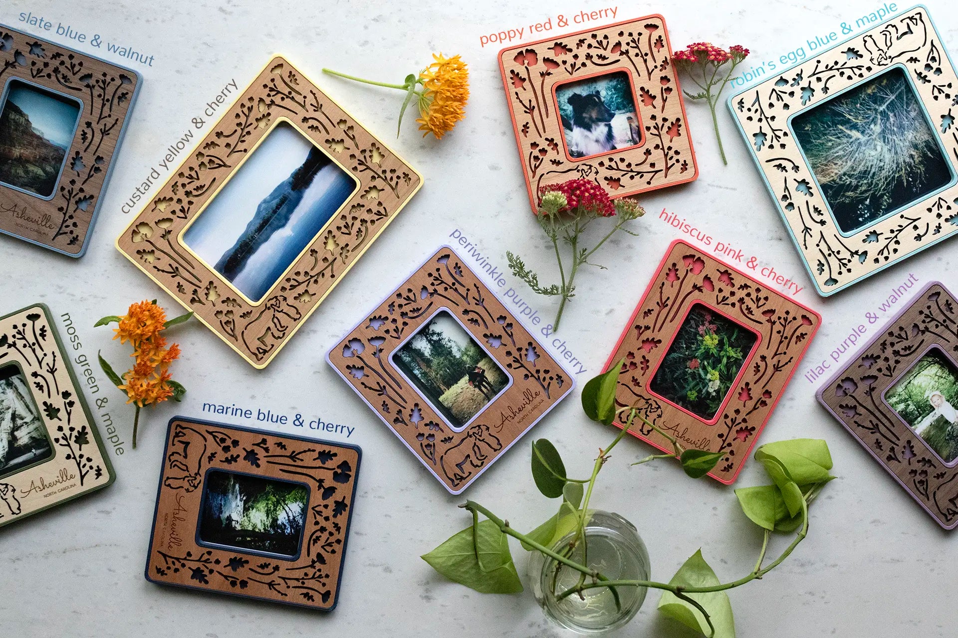 An assortment of colorful, laser cut Polaroid frames with mama and baby bear woodlands design. The frames are lying on a white surface, surrounded by flowers from the garden. They have an intricate, feminine design and real wooden inlays.