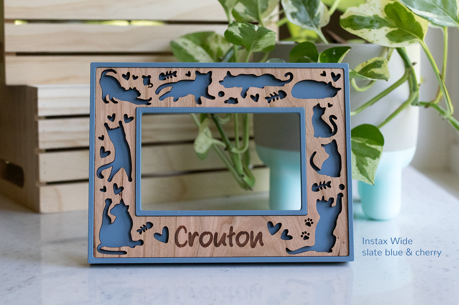 Personalized cat frame with the name "Crouton" engraved on the bottom. The frame fits Instax Wide photos and has a blue frame with cherry wood insert. The frame can be customized with your cat's name or a heartfelt message.