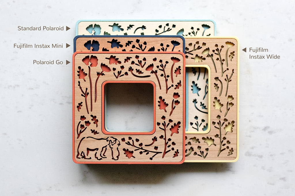 A selection of magnetic frames in various sizes: Polaroid Go, Standard Polaroid, Instax Mini, and Instax Wide. For size comparison, the Instax Mini frame is roughly the size of a standard credit card. The frames display a beautiful laser cut design of woodland flowers and bears hugging.