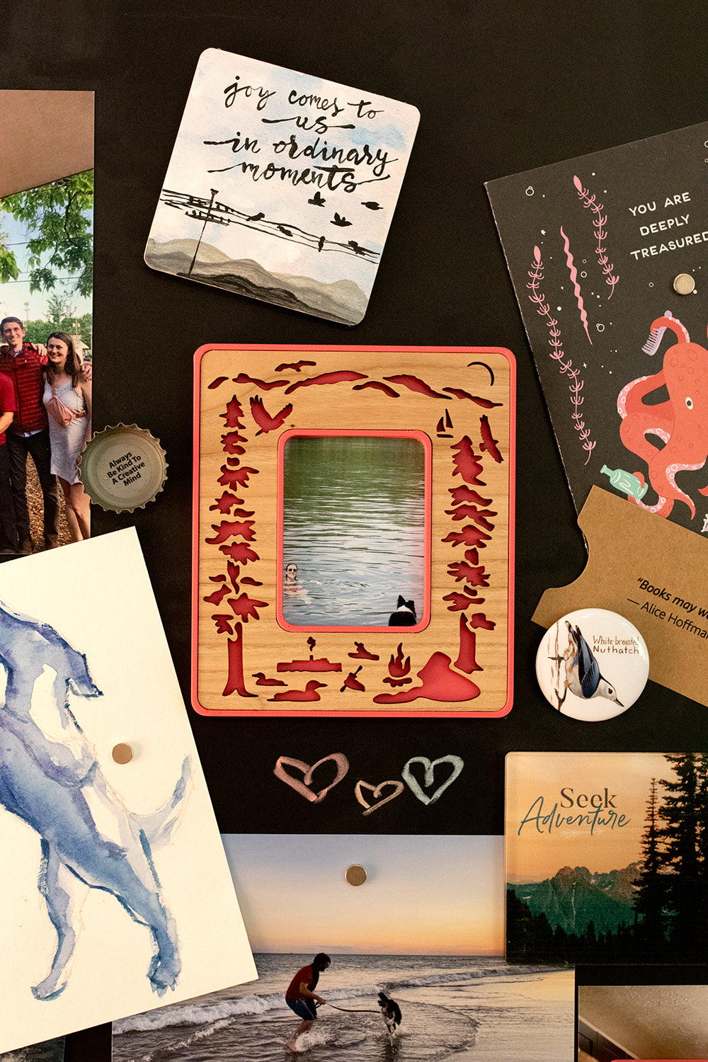 A Lake George NY magnetic Polaroid photo frame for Instax Mini hanging on a black, magnetic chalkboard. The frame has a cherry inlay and a bright pink border. The frame is surrounded by travel inspired postcards and photographs. This mini picture frame has a unique laser cut design.