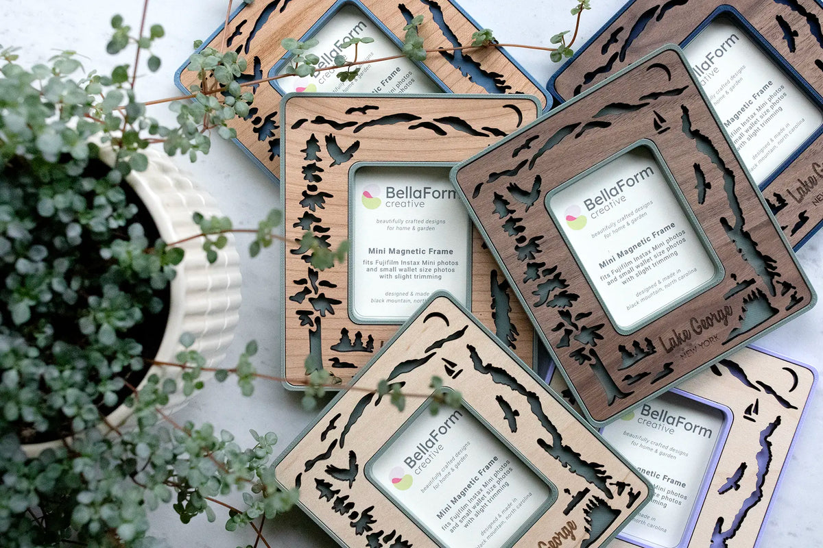 Laser-cut Lake George magnetic frames with wooden inlays. Frames feature the silhouette of Lake George New York, Adirondack mountains in the distance, loons on the lake, osprey flying in the sky, evergreens on islands in the lake, the Lac Du Saint Sacrement tour boat, and a pair of kayakers.