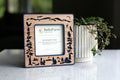 A standard Polaroid frame with dark blue plastic housing and laser cut cherry inlay. The frame has magnets on the back and is sitting next to a houseplant. The frame displays a card that reads "BellaForm Creative, Mini Magnetic Frame". The Polaroid frame fits standard 600 / SX-70 / iType photos.