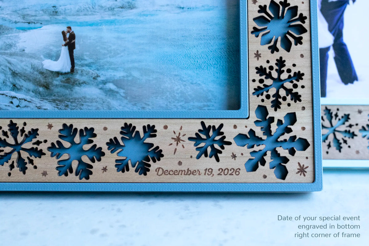 Close-up view of a personalized wedding keepsake frame for winter weddings. The wedding date is engraved in the bottom right corner of the frame. The frame has a blue frame housing and cherry wood inlay with delicate laser-cut snowflakes all around.