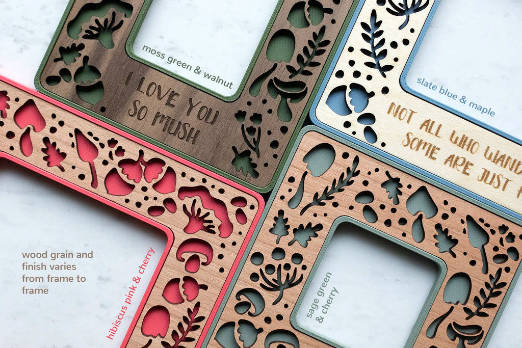 A close-up, detail view of four mini frames with unique mushroom designs, in various colors, including pink, moss green, sage green, and slate blue. The bottom left corner of the image reads "wood grain and finish varies from frame to frame". Personalized mushroom gifts.