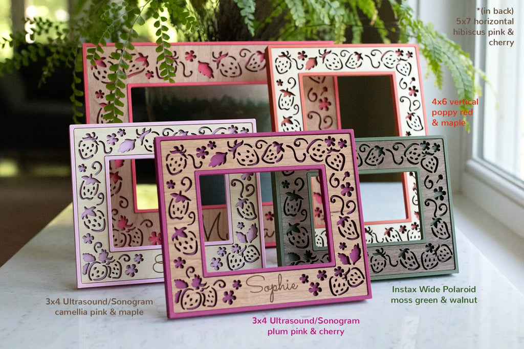 An assortment of five laser cut strawberry frames in various shades of red, pink, and green. The frames have dark walnut, light maple, and cherry wooden inlays. The frame housings are 3D printed using a lightweight material, and the inlays are made from real wood to add warmth and natural aesthetic.