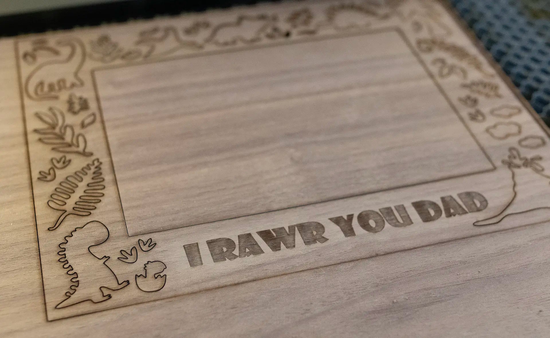 Laser cutting process to create custom wooden picture frames. A piece of walnut plywood being cut on a laser cutter to make a dinosaur picture frame with custom engraving "I Rawr You Dad."